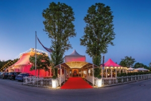 Ein rot beleuchtetes Zirkuszelt mit zwei großen Bäumen am Eingang für die Veranstaltung Magie in München als Eventtipp von unserem zentralen Hotel am Münchener Hauptbahnhof